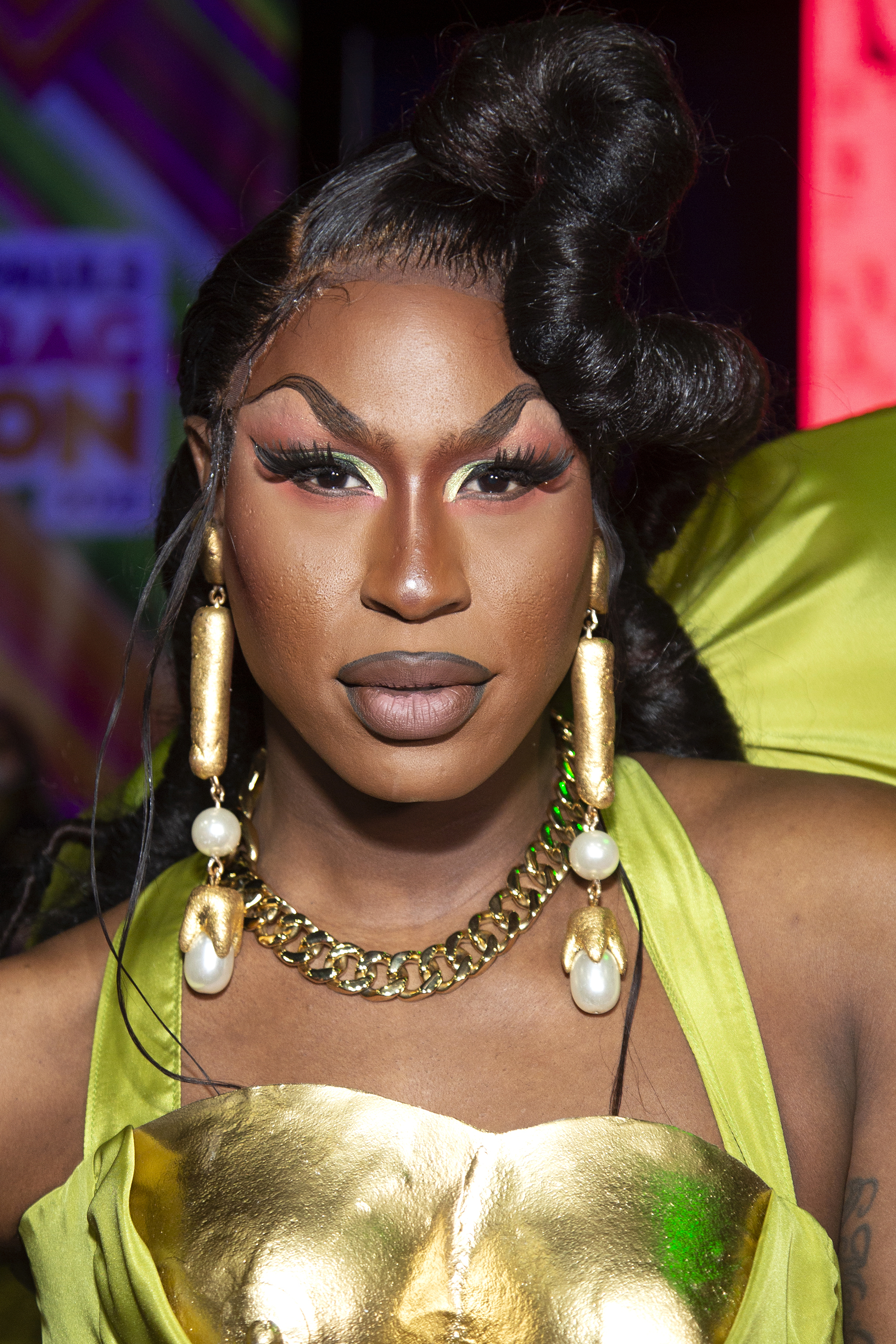 Shea with an elaborate updo, bold makeup, large earrings, and a metal-plated outfit at an event