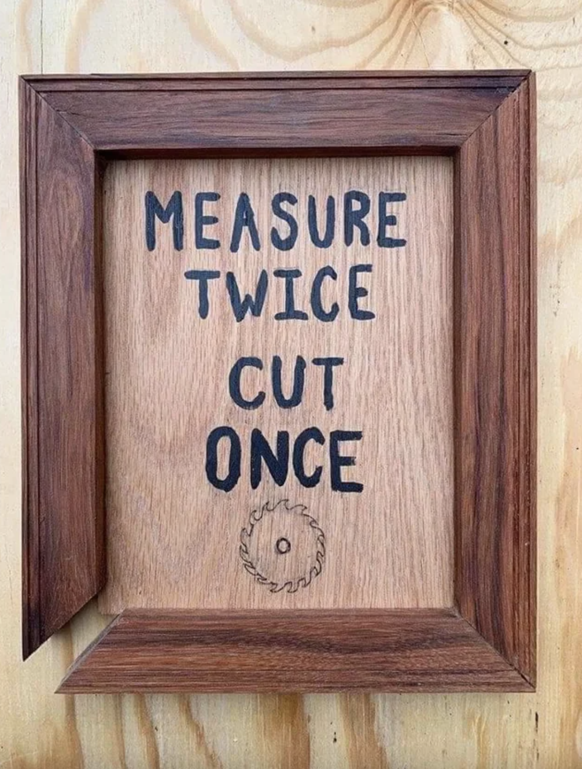 Wooden framed sign with text &quot;MEASURE TWICE CUT ONCE&quot; above a saw blade illustration