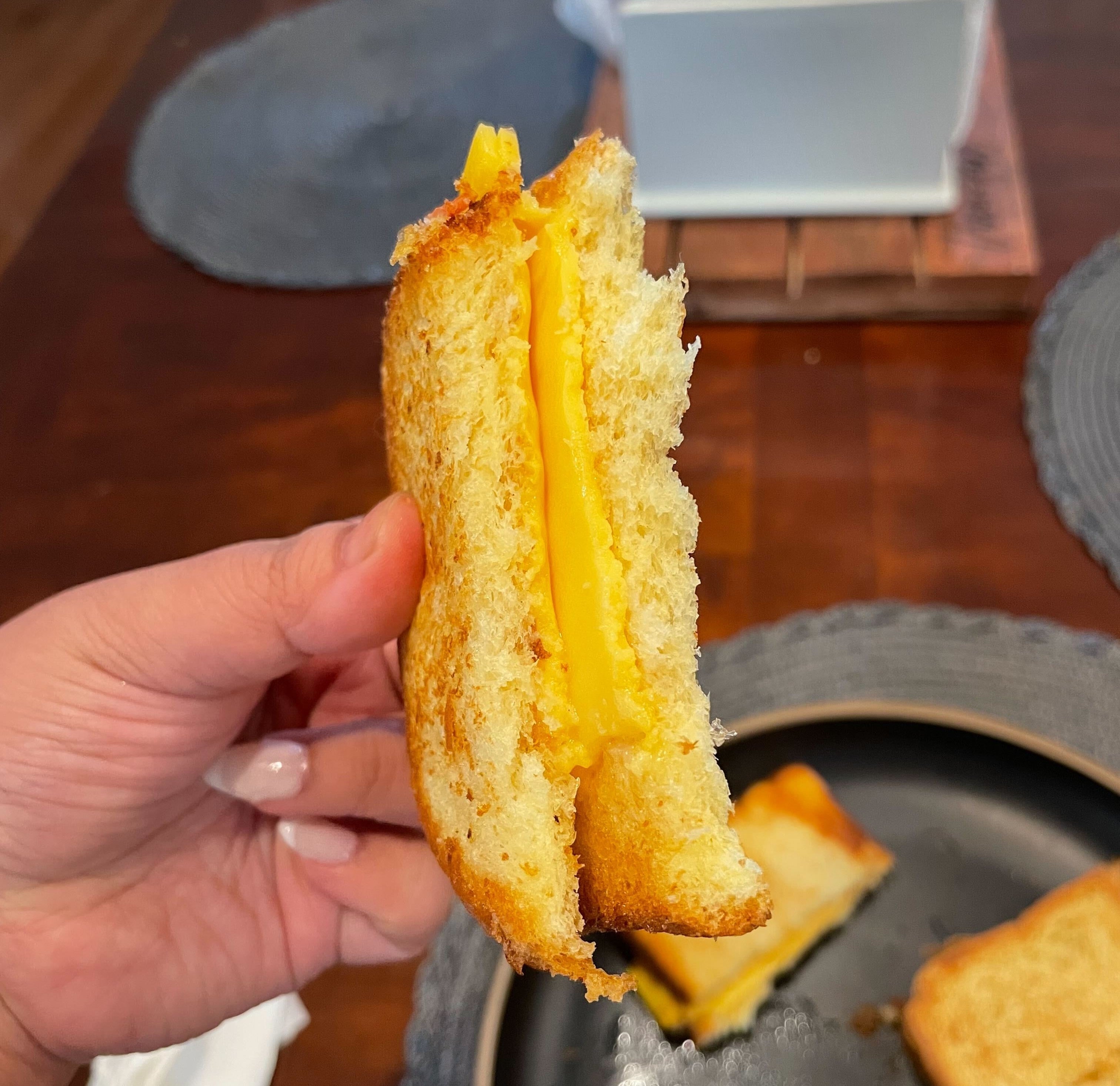 Person holding a half-eaten grilled cheese sandwich, with not-so-melted cheese visible