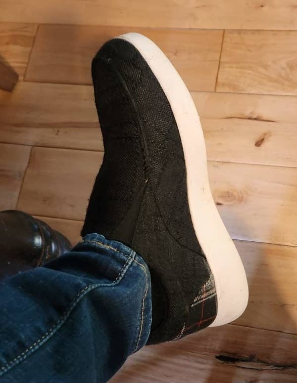 a reviewer in jeans wearing a black shoe with a white sole, resting foot on chair leg