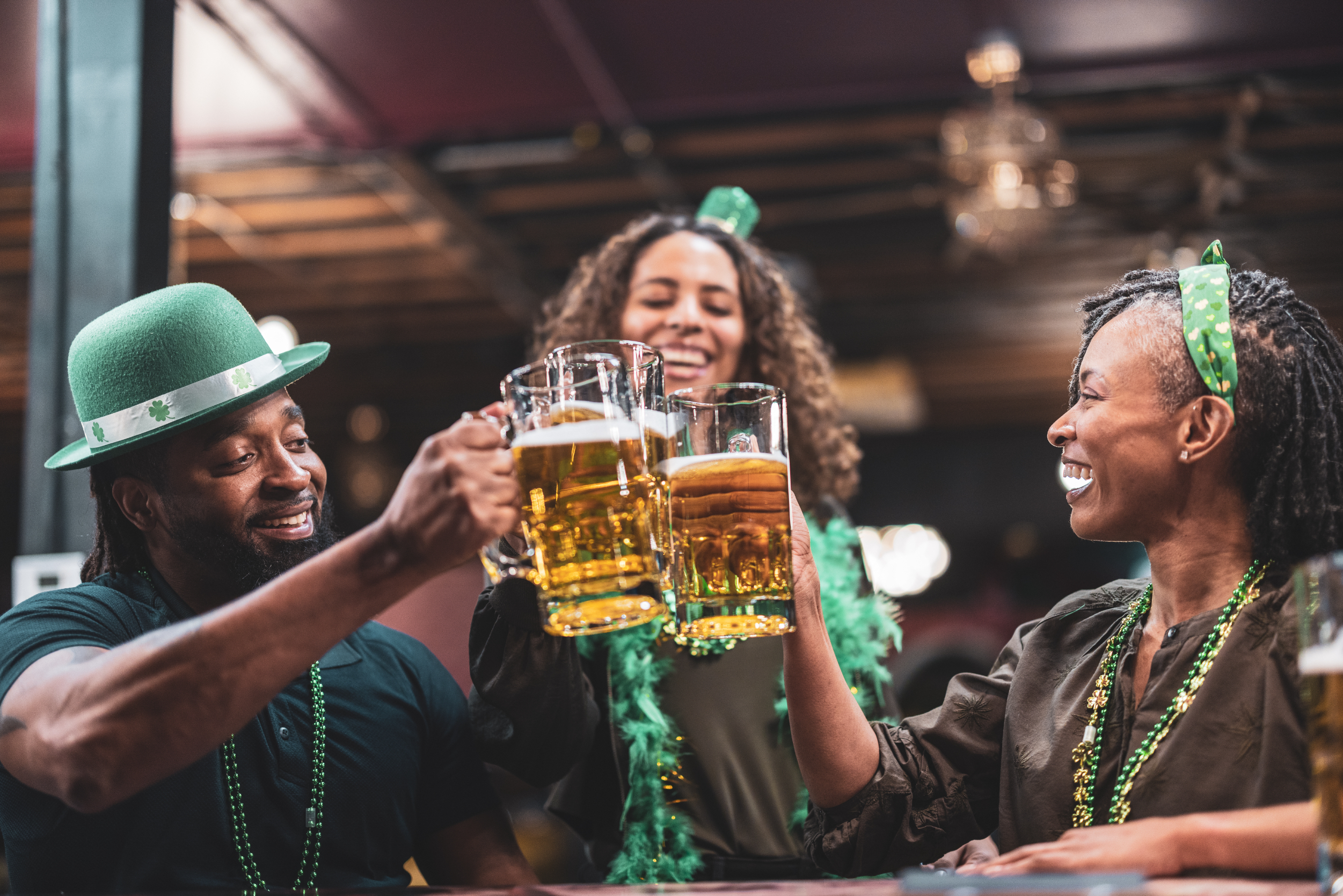 Three people celebrating, wearing St. Patrick&#x27;s Day accessories, toasting with beer