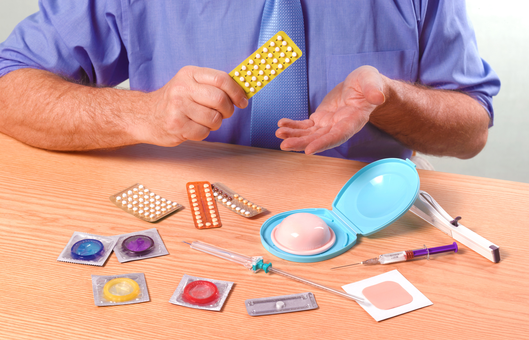 Person at a table with various contraceptives, including pills, condoms, and injections