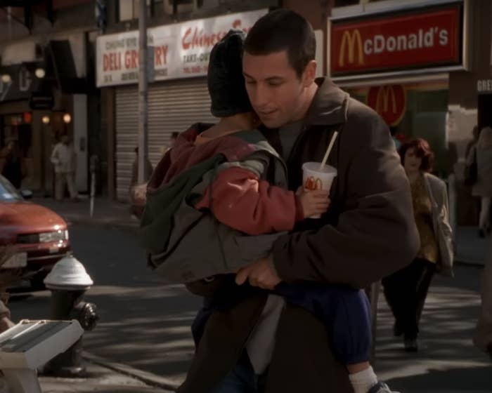 Man carrying a child in an urban setting with a McDonald&#x27;s cup in hand