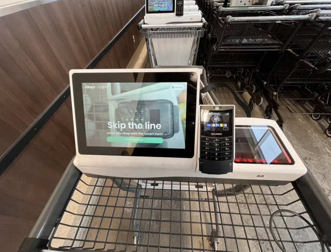 Self-checkout screen on a shopping cart with &quot;Skip the line&quot; prompt and a payment terminal beside it