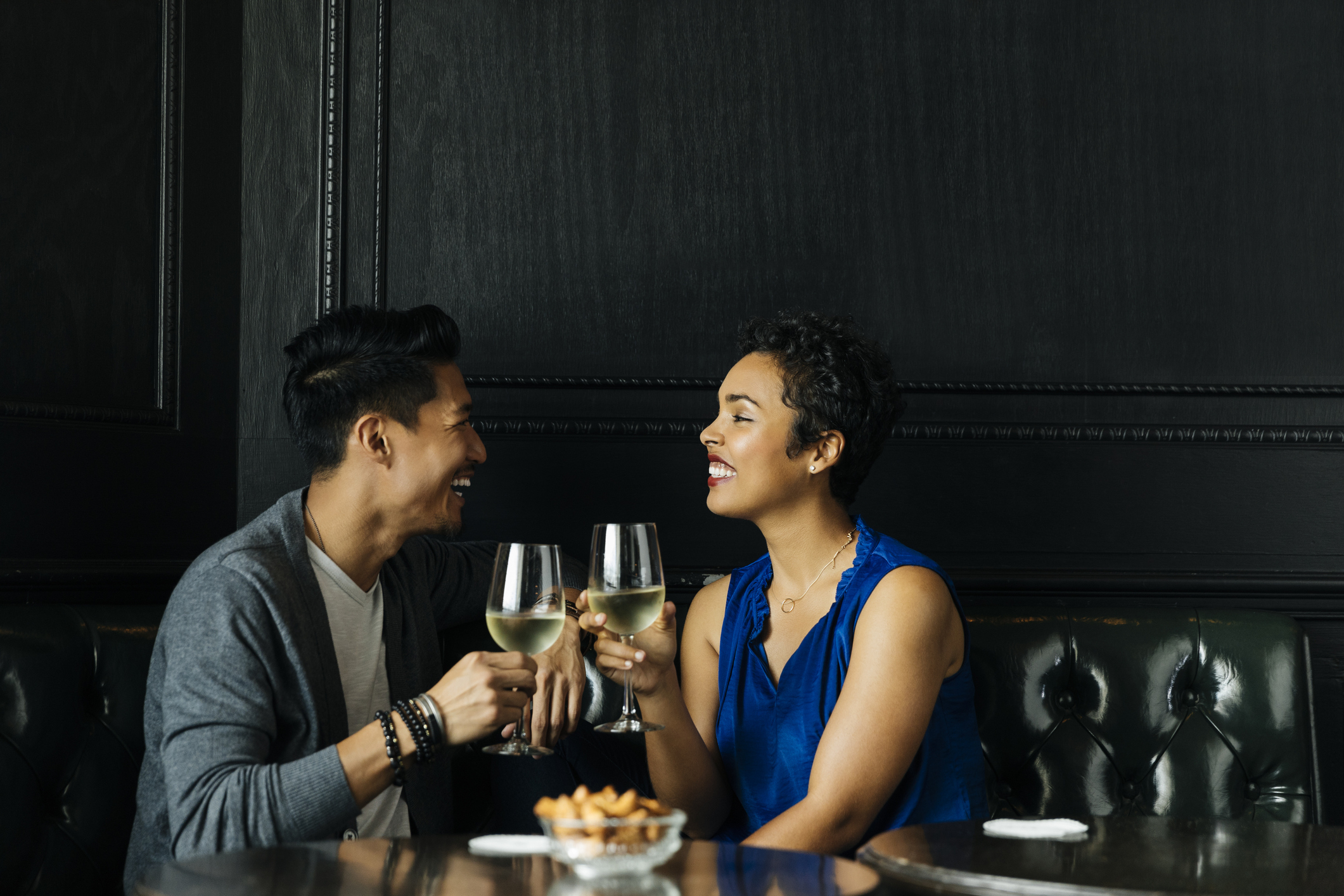 Two people smiling at each other while holding wine glasses in a dimly lit room