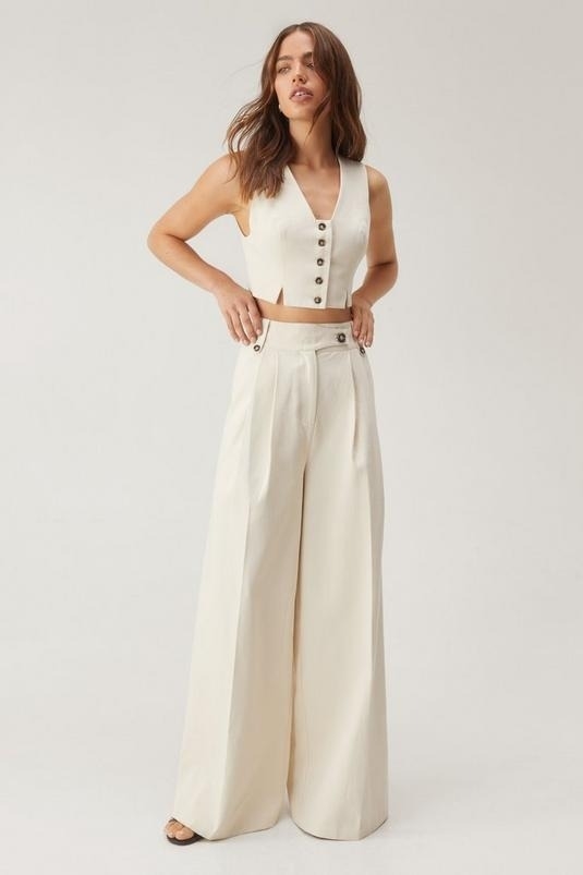 Woman in a white sleeveless crop top with button details and high-waisted wide-leg pants