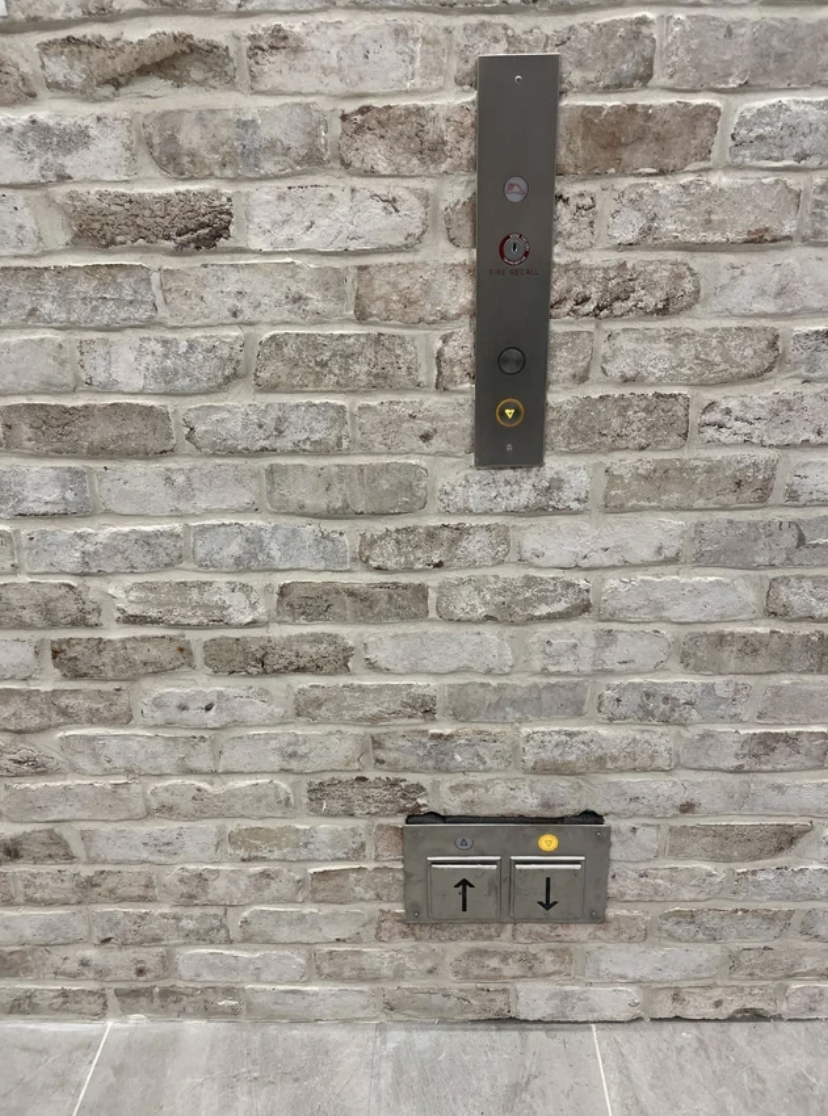 Elevator buttons and braille on a brick wall, indicating floor levels with up and down arrows