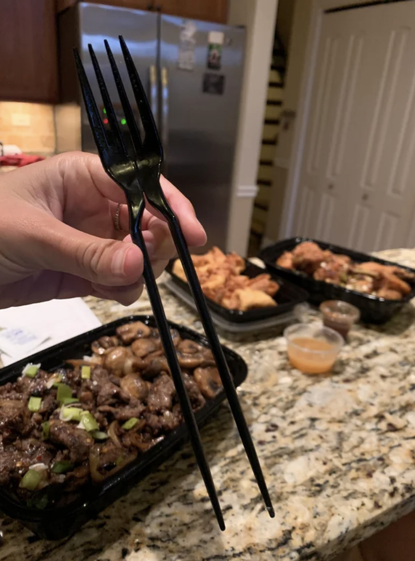 Hand holding a bent fork with takeout food containers in the background