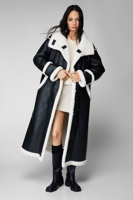 Model wears a long black and white shearling coat with black boots