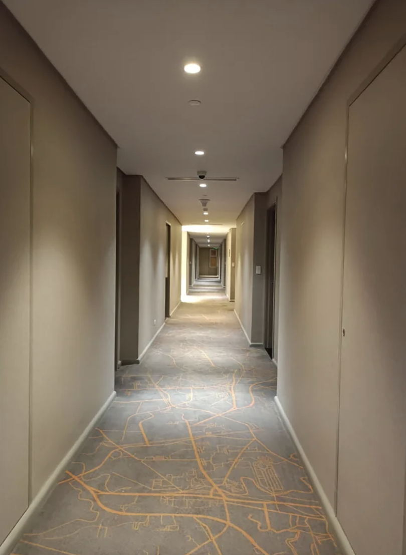 A long, narrow hotel corridor with a map on the carpet