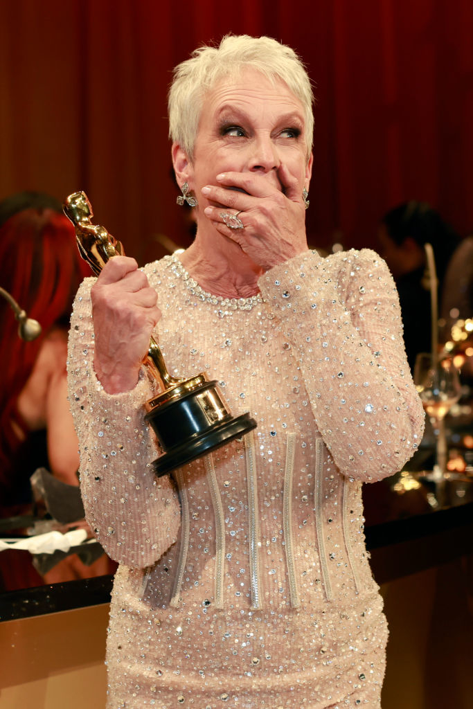 Jamie in beaded gown holding an Oscar, looking surprised or emotional