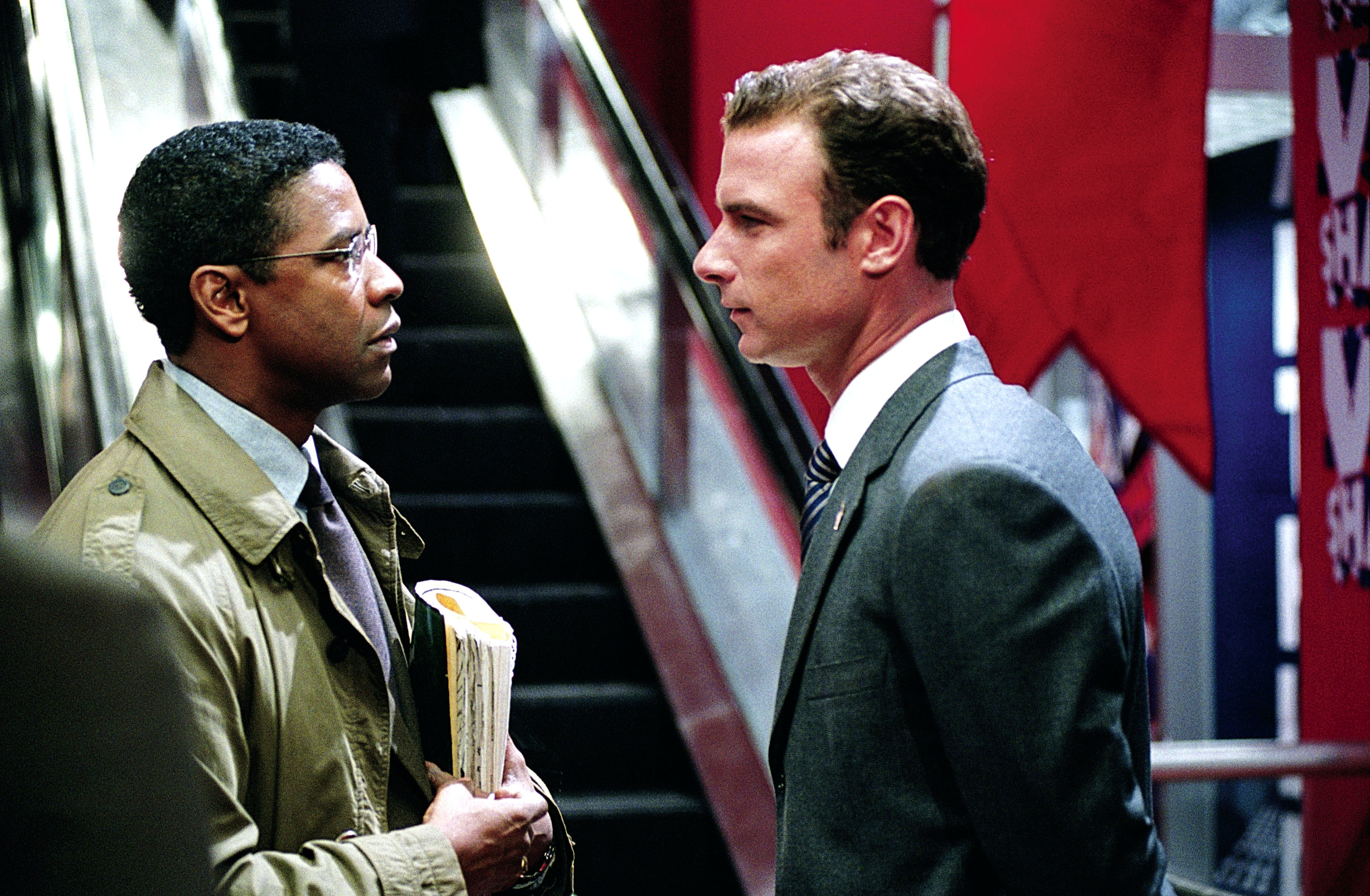 Denzel Washington and Liev Schreiber in a serious conversation, one in a trench coat, the other in a suit and tie