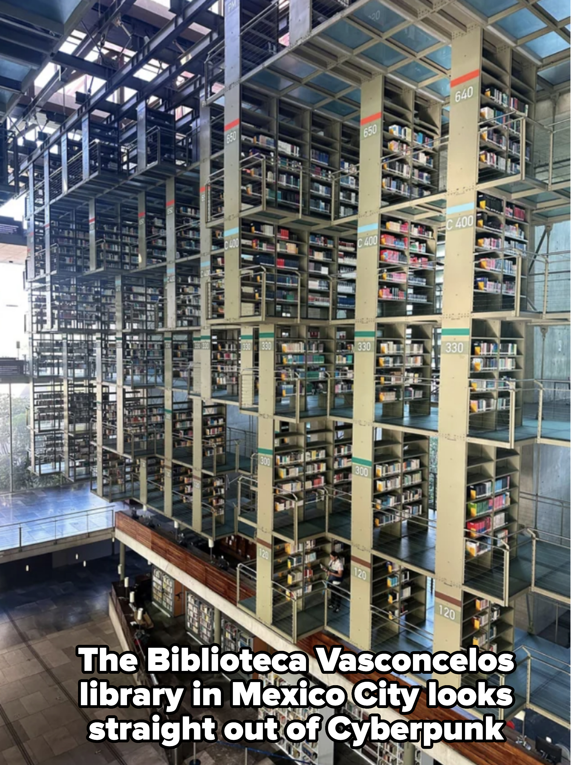 Multi-level library shelves filled with books, accessing walkways and labeled columns