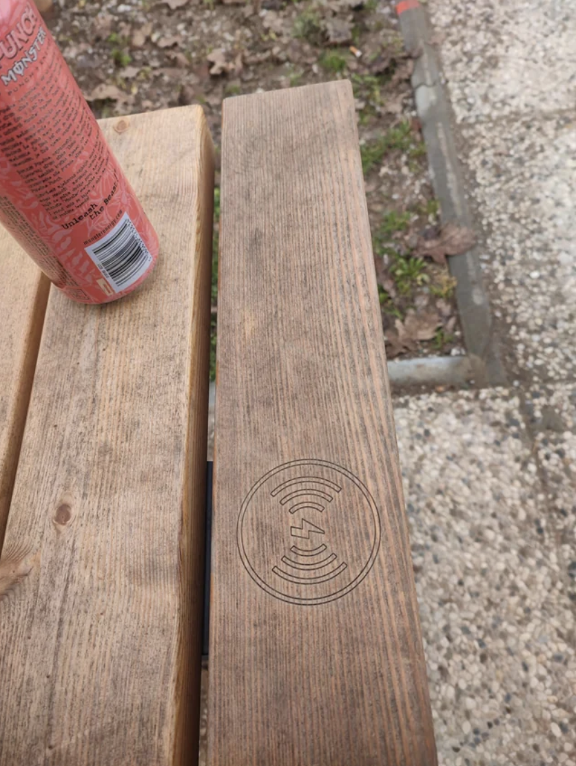 Wooden plank with a burned-in Wi-Fi symbol, next to a spray can, on an outdoor bench