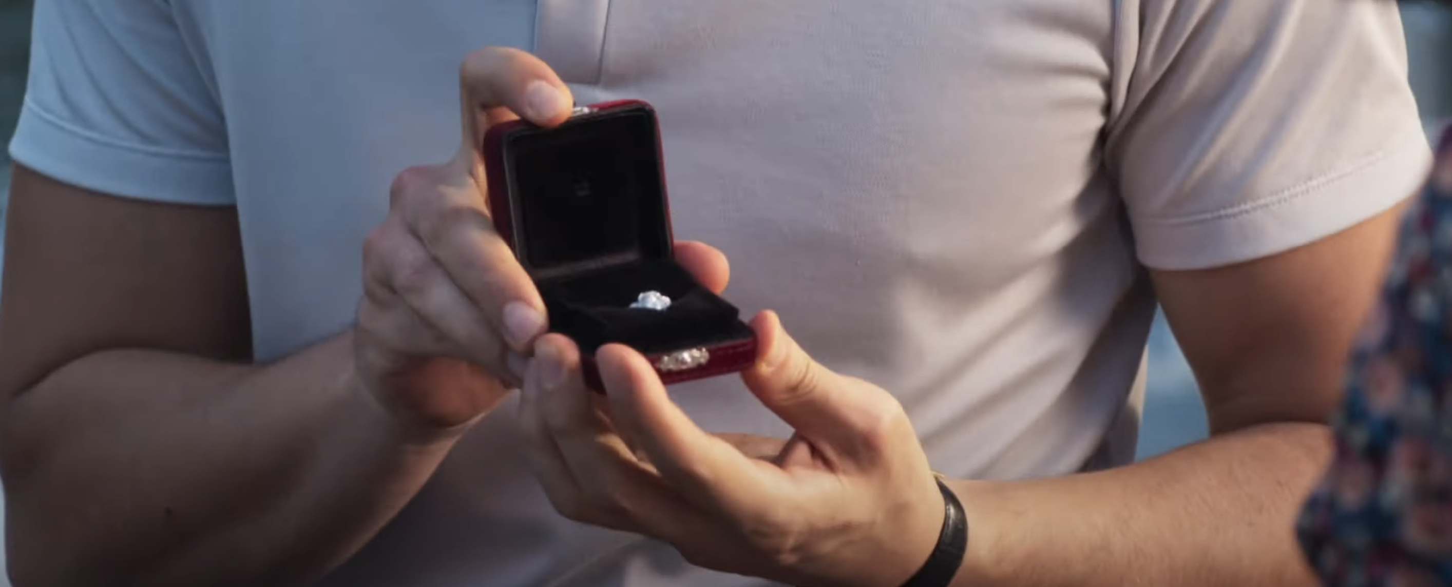 Close-up of a person holding an open ring box with an engagement ring