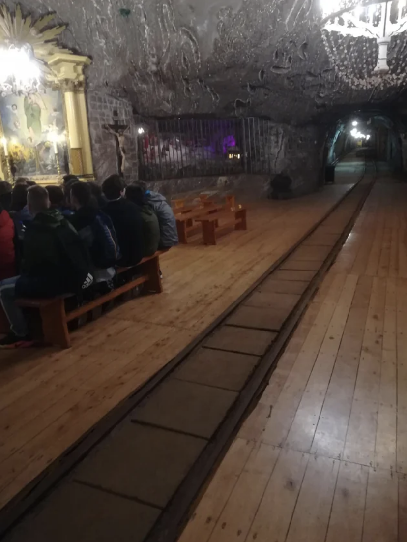 Visitors seated on benches in a dimly lit underground salt mine chapel with ornate carvings
