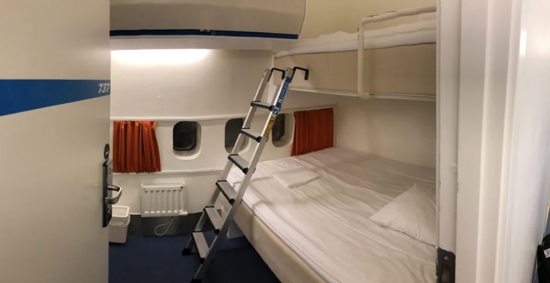 A compact cruise ship cabin with an upper and lower bunk bed and ladder