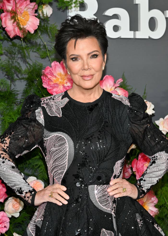 Kris Jenner posing with her hands on her hips in a detailed gown with floral accents at an event