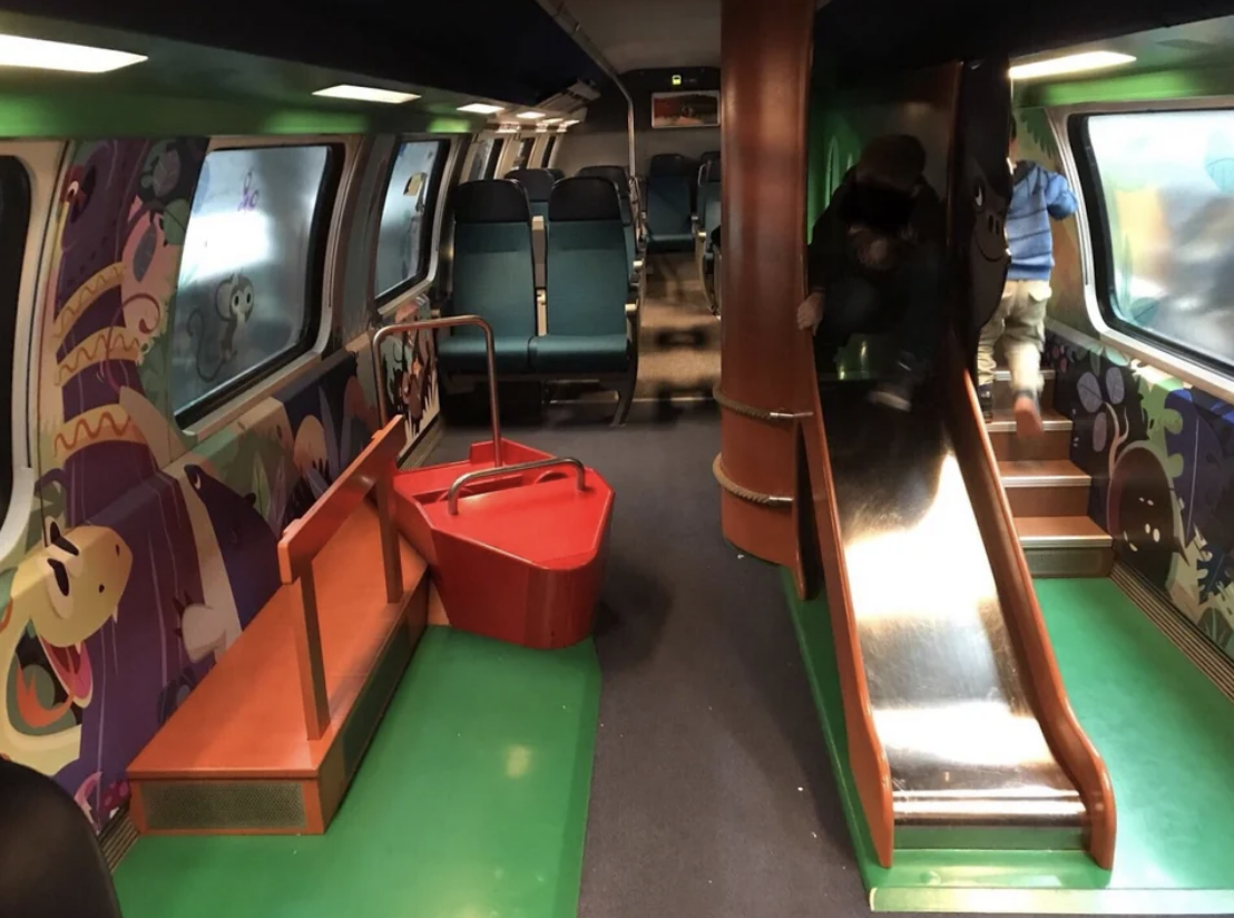 Children&#x27;s play area inside a train carriage with seats, a slide, and playful decorations