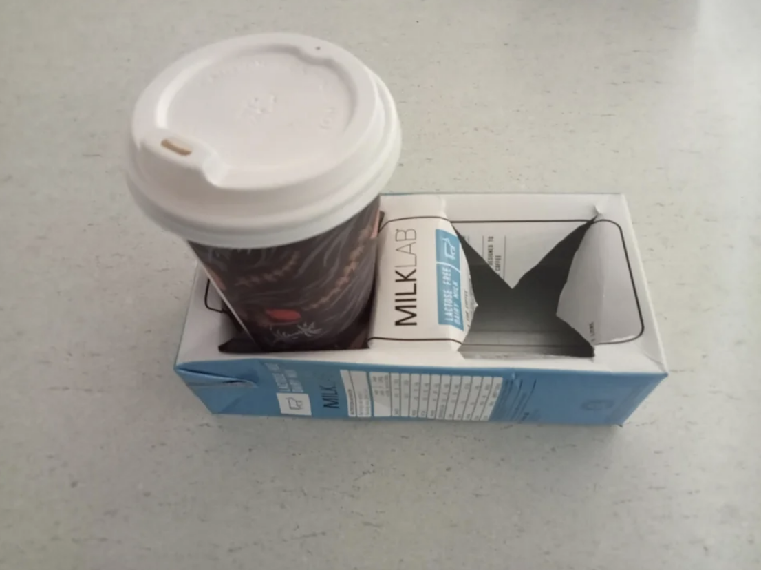 A coffee cup atop a carton of MILKLAB almond milk on a counter