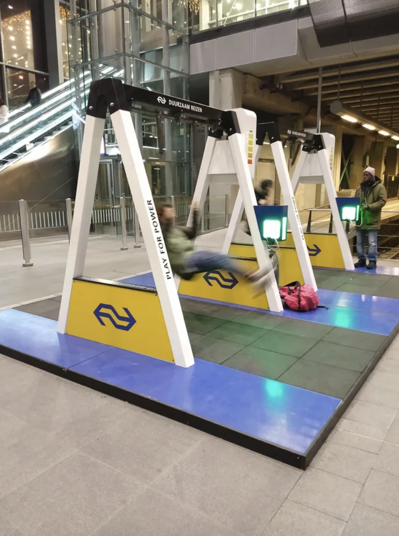 A person is swinging on an indoor public swing set with a logo that reads &quot;NS&quot; at a train station