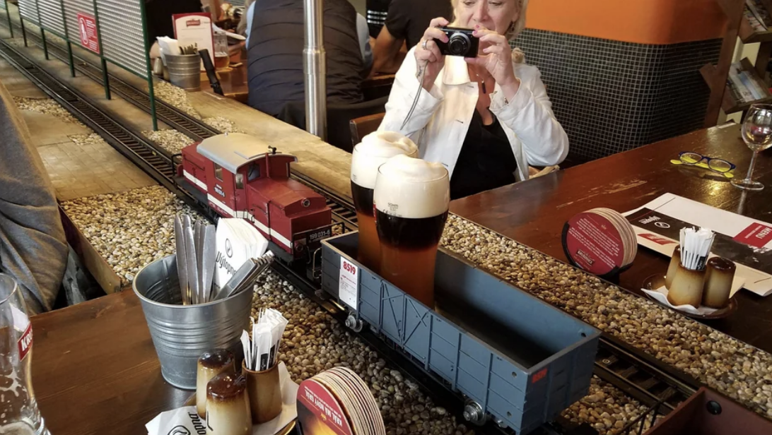 A model train delivering drinks on a track in a restaurant, with a person photographing it