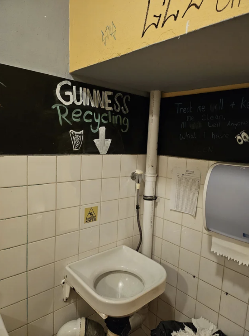 Public restroom with writings and a drawing on wall above toilet, hand dryer to the right