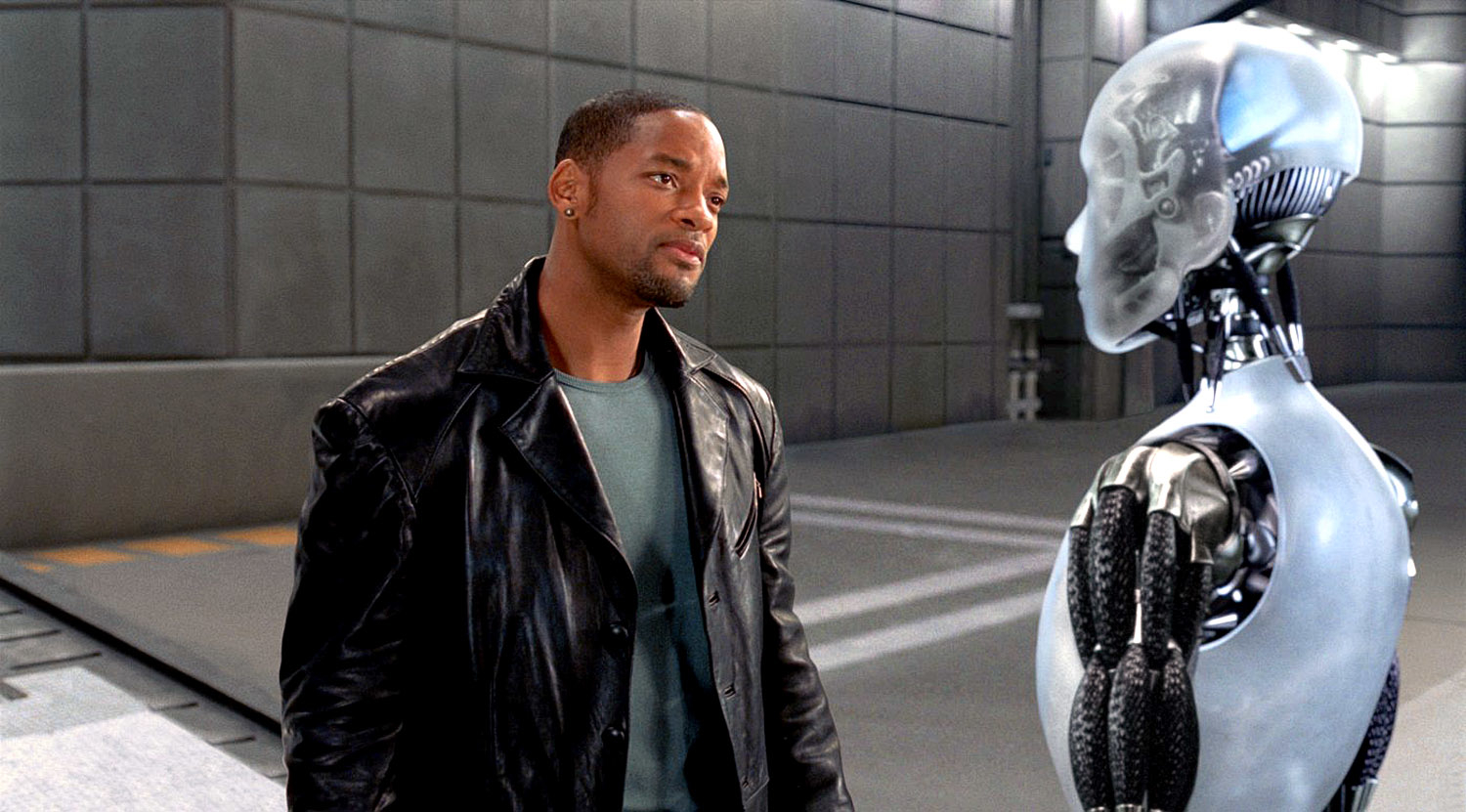 Will Smith, in a leather jacket, converses with a humanoid robot in a futuristic setting