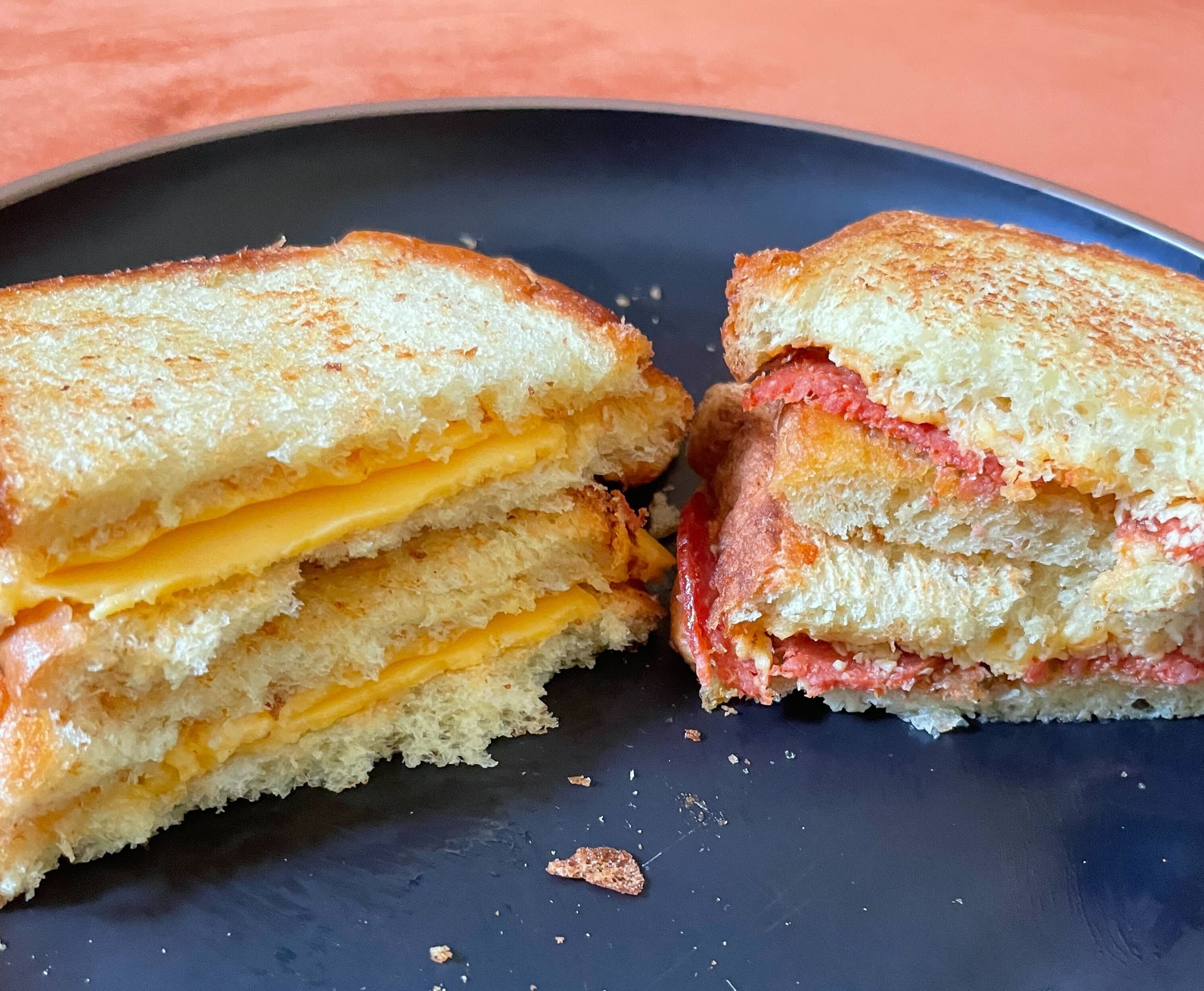 Grilled cheese sandwiches cut in half on a plate, one with pepperoni