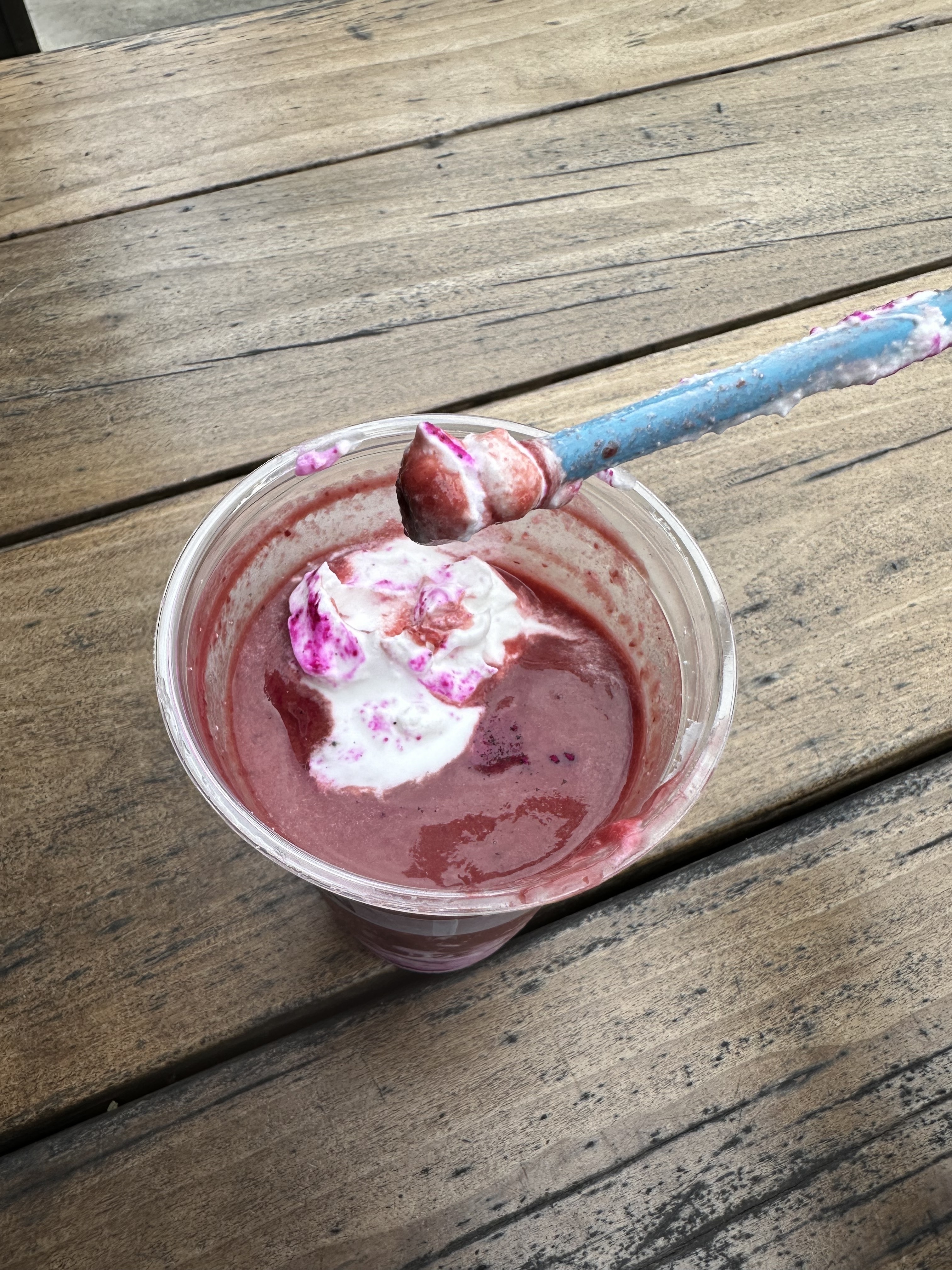 A cup of mixed berry smoothie with a spoon, on a wooden table