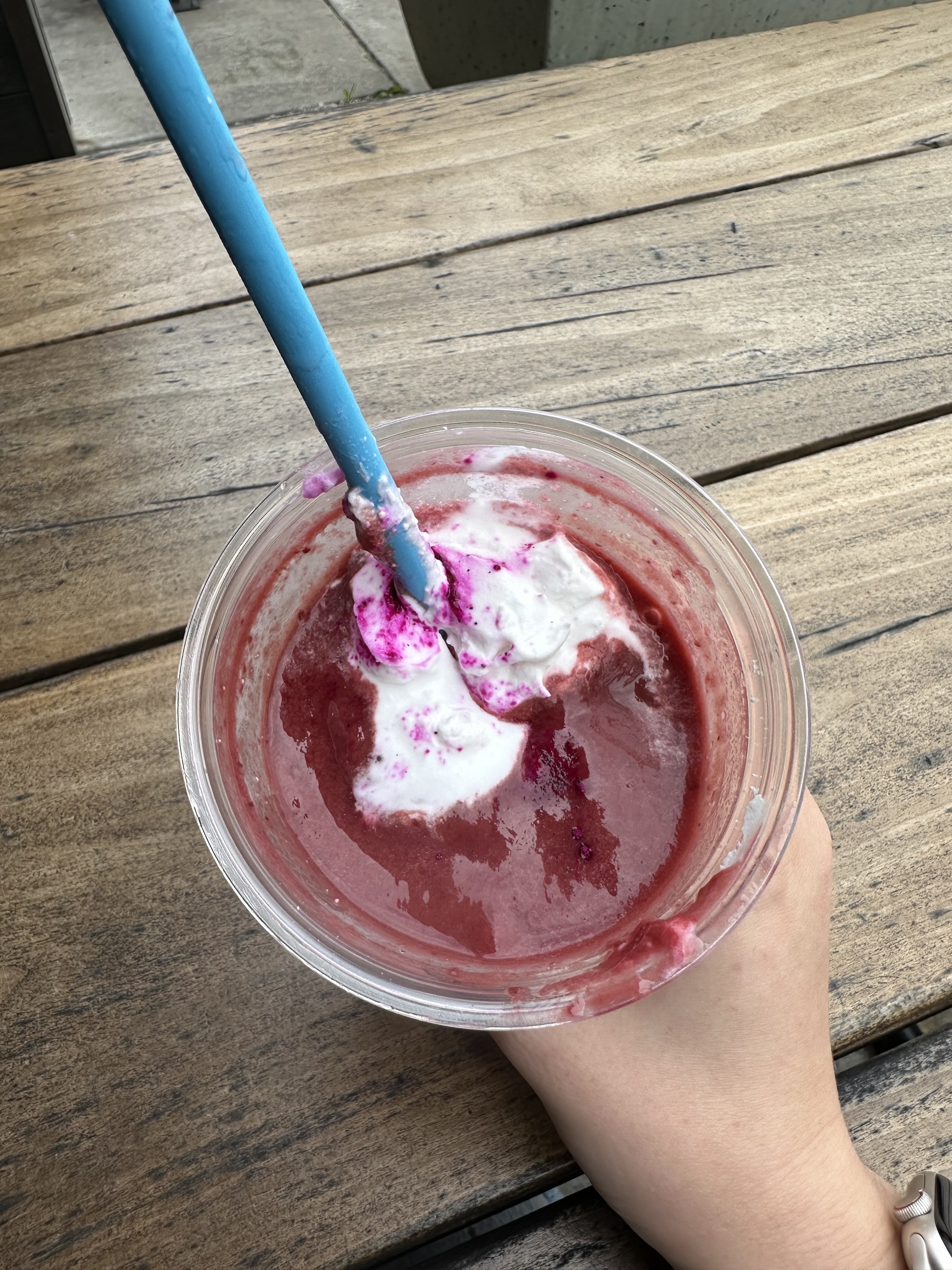 Top view of a hand holding a smoothie with a blue straw, on a wooden table