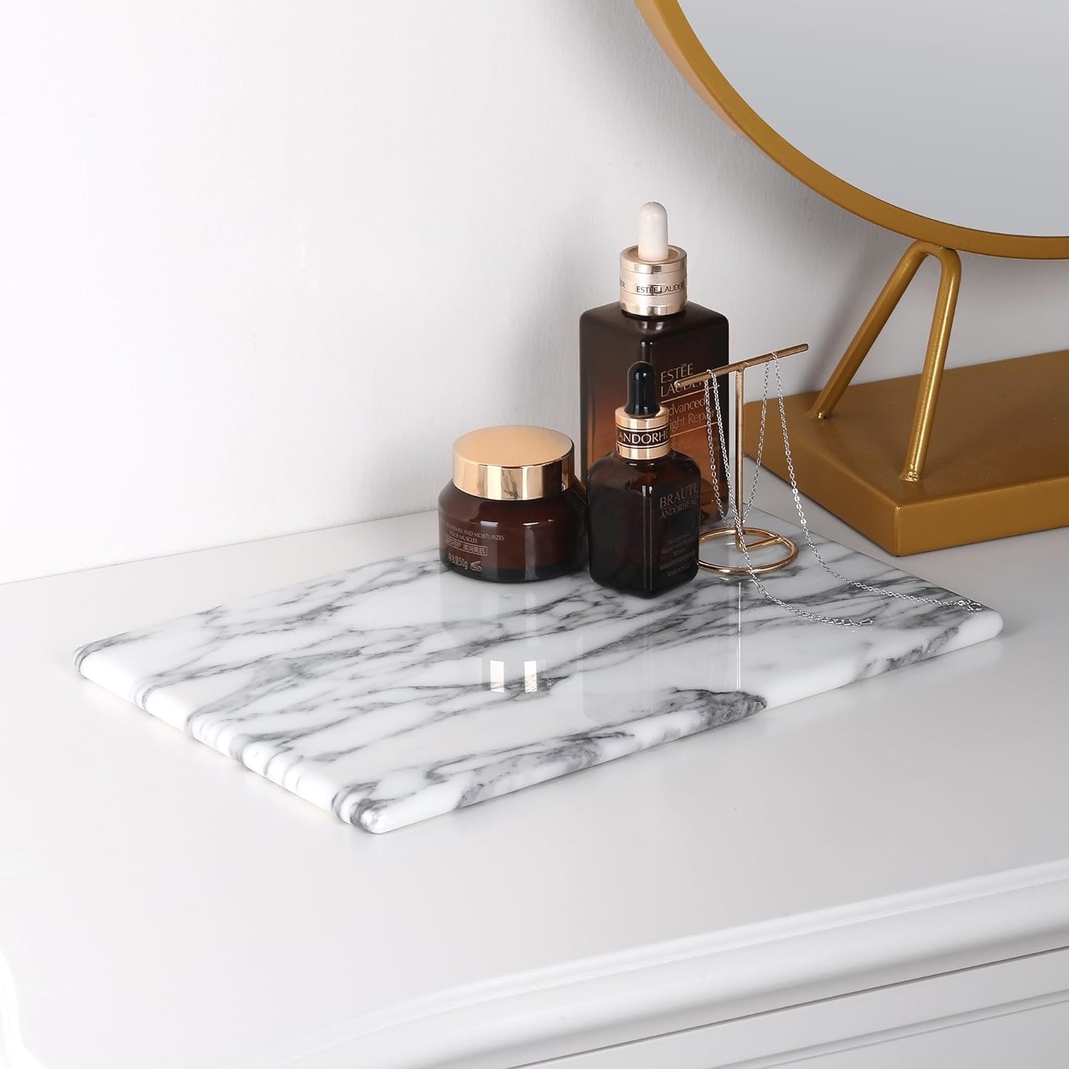 A marble tray with skincare products and a necklace on a vanity