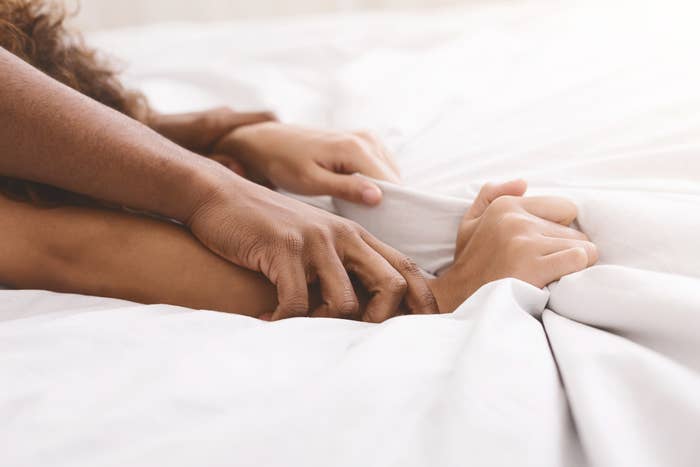 Two people holding hands on a bed, suggesting intimacy and connection