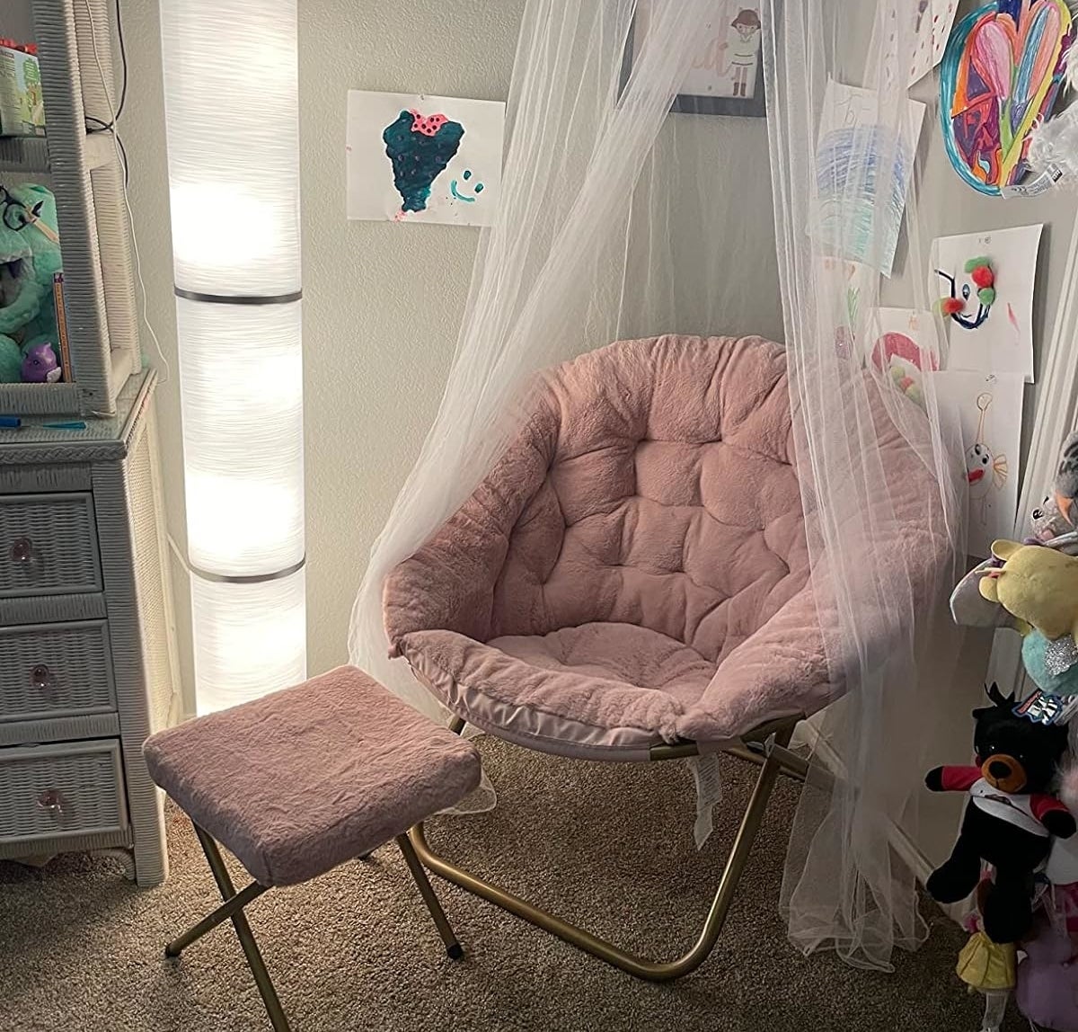 A cozy reading nook with a plush round chair, a small stool, and a floor lamp, adorned with children&#x27;s artwork