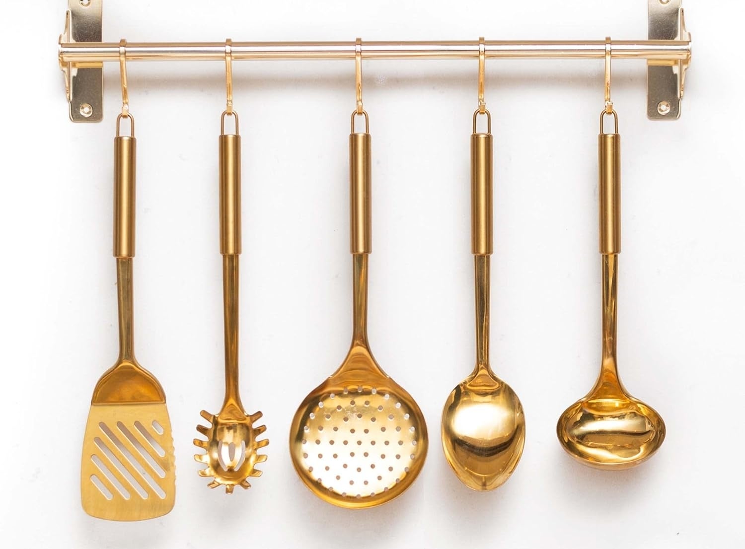 Five brass kitchen utensils hanging on a rack