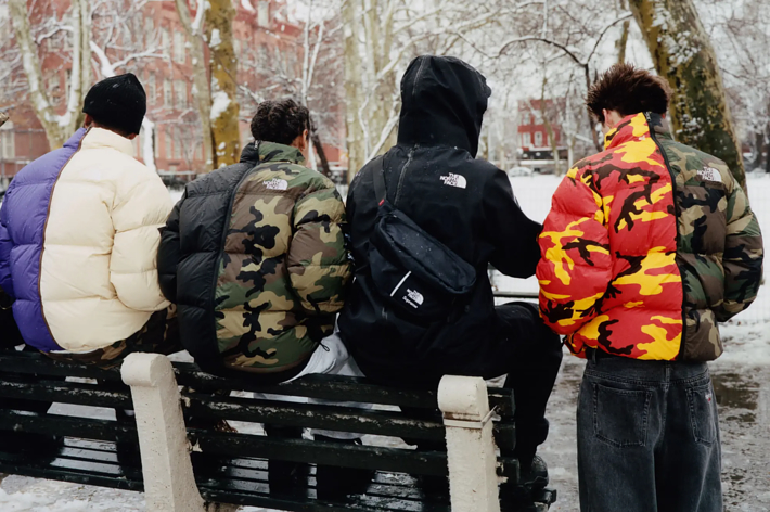 Four individuals seated on a bench wearing winter jackets with camouflage patterns