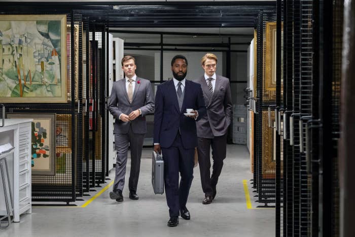 Scene from Tenet: Three men in business attire walk in an art storage room