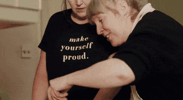 Two people interacting, one wears a shirt with the text &quot;make yourself proud.&quot;