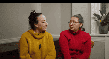 Two women sitting and conversing, one in a yellow sweater and the other in a red turtleneck
