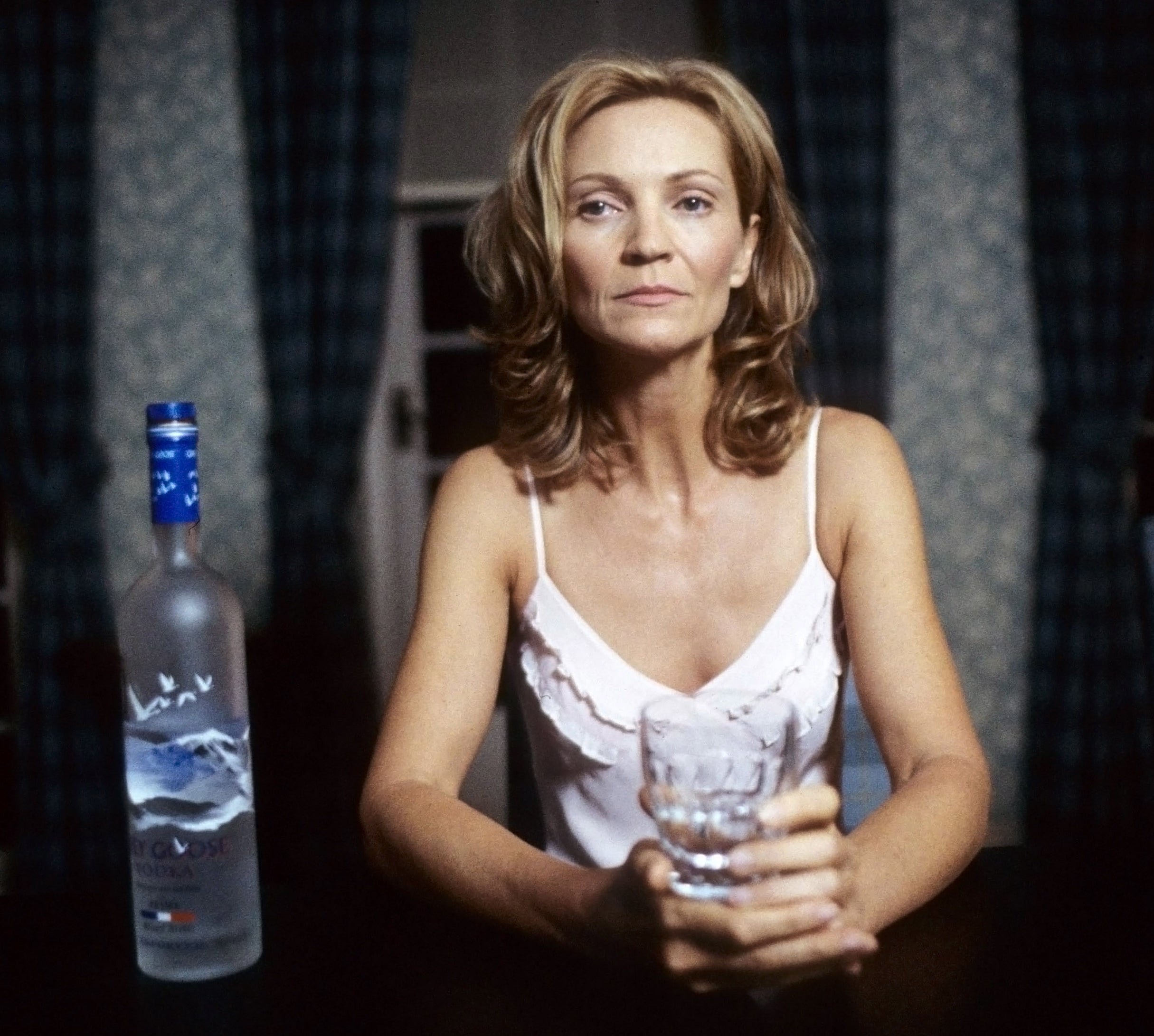 Closeup of a woman with a drink in her hand and a bottle of vodka next to her