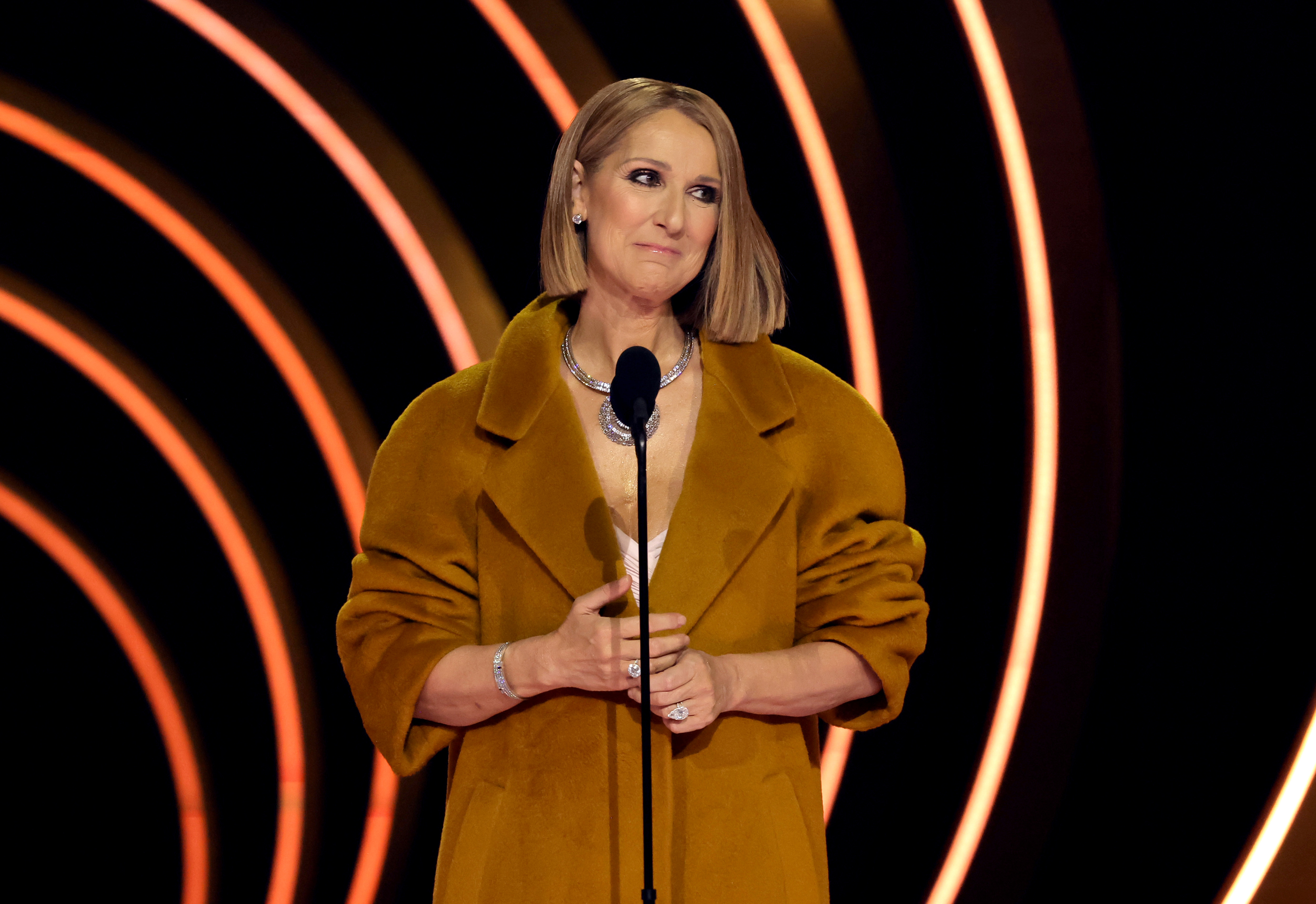 Close-up of Céline smiling onstage at the Grammys in a long coat and gown