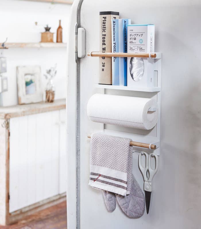 the steel white and wood magnetic fridge rack hanging in a kitchen holding paper towels, scissors, oven mitt, and other items