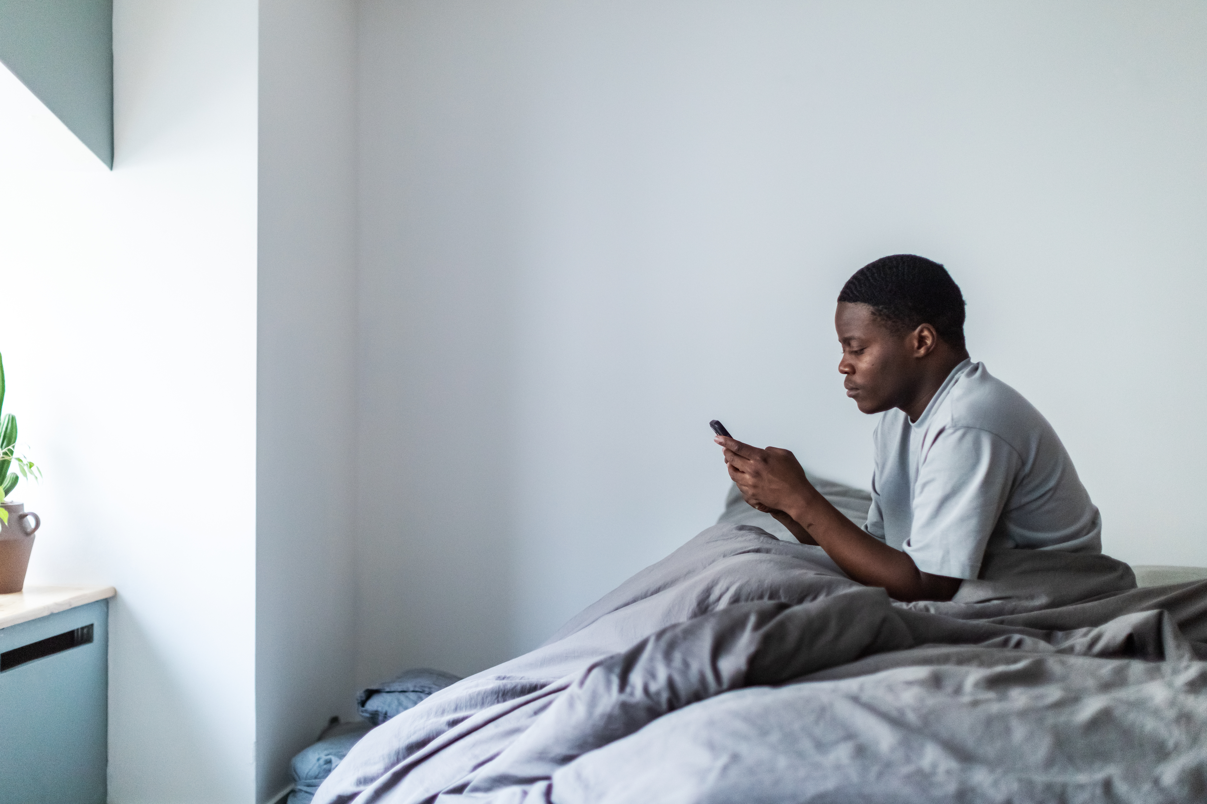 A depressed young man looking at his phone in bed
