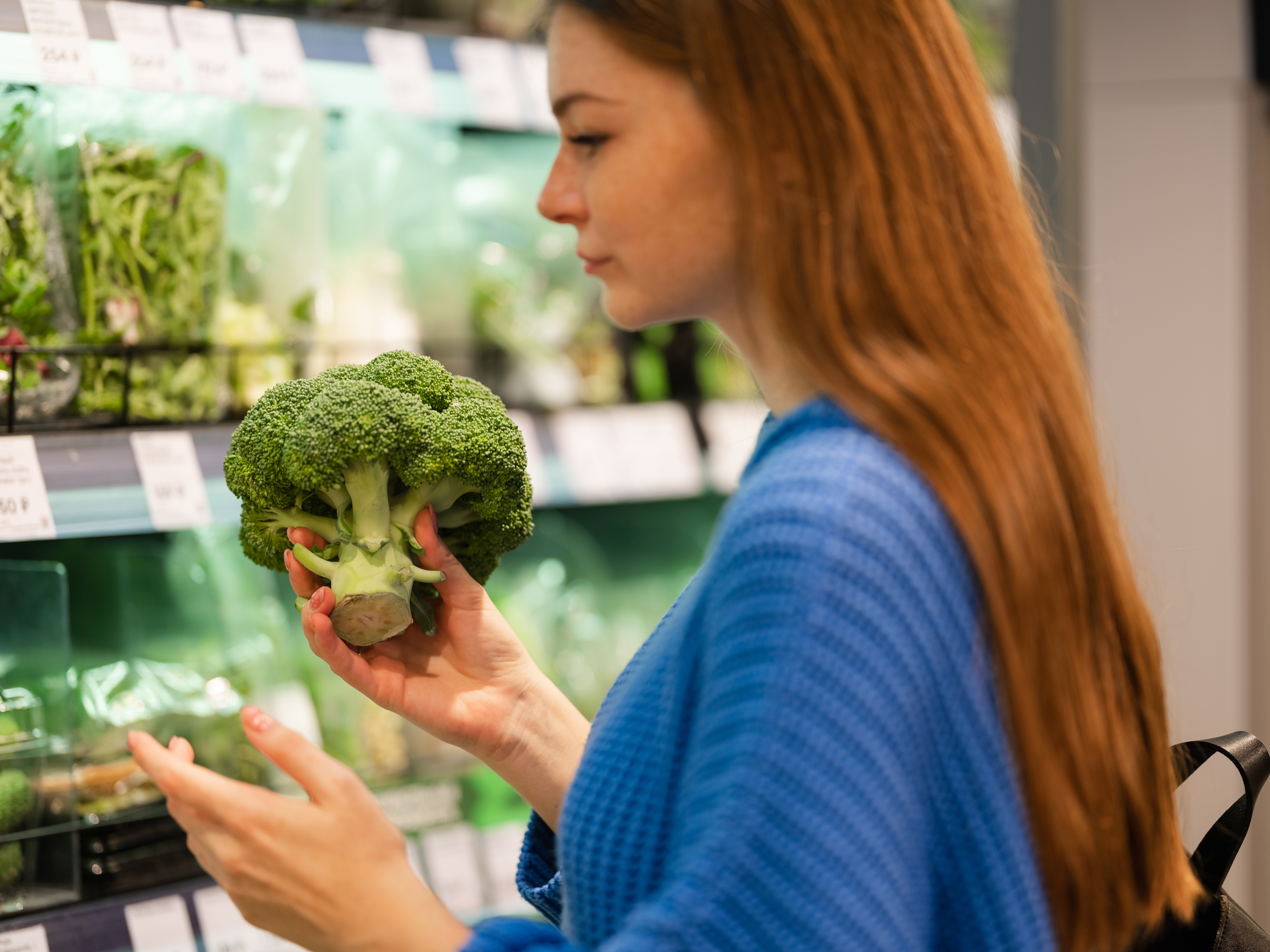 woman shopping for produce holding a broccoli