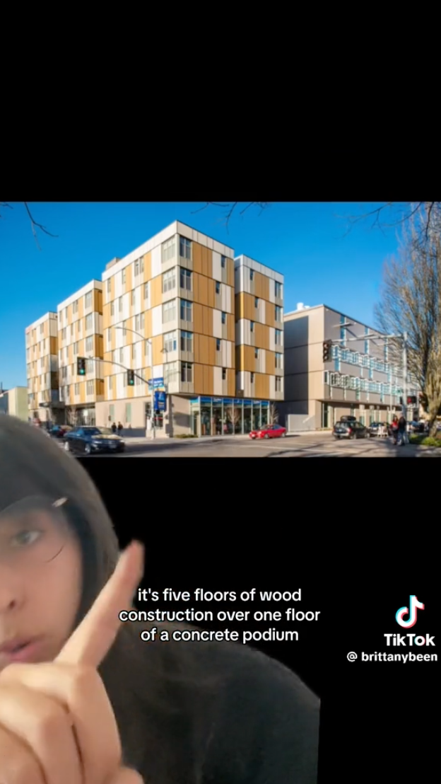 Brittany in front of a five-over-one building saying &quot;It&#x27;s five floor of wood construction over one floor of a concrete podium&quot;