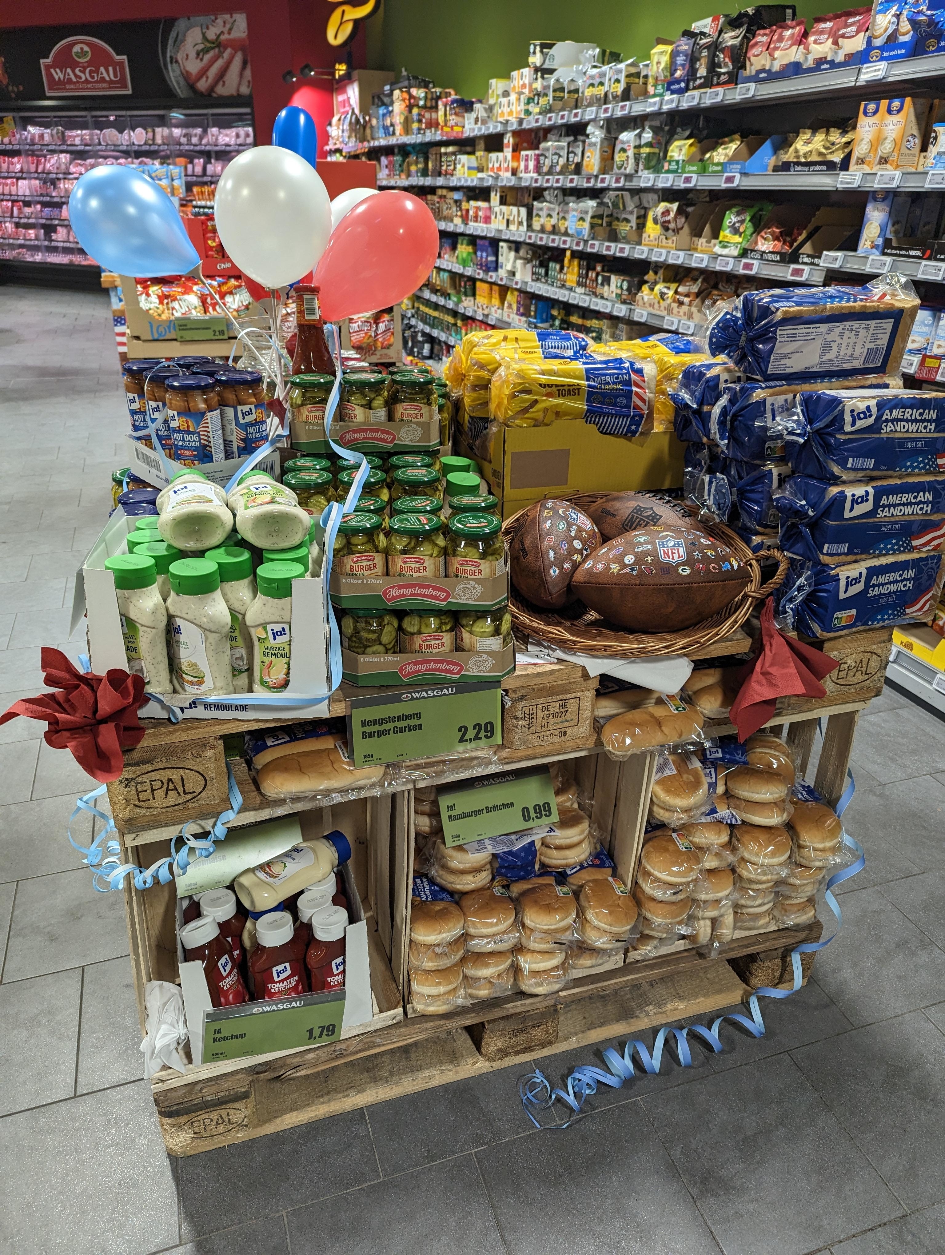 A store display with hamburger buns, ketchup, loaves of bread, pickles, hot dogs, and other condiments