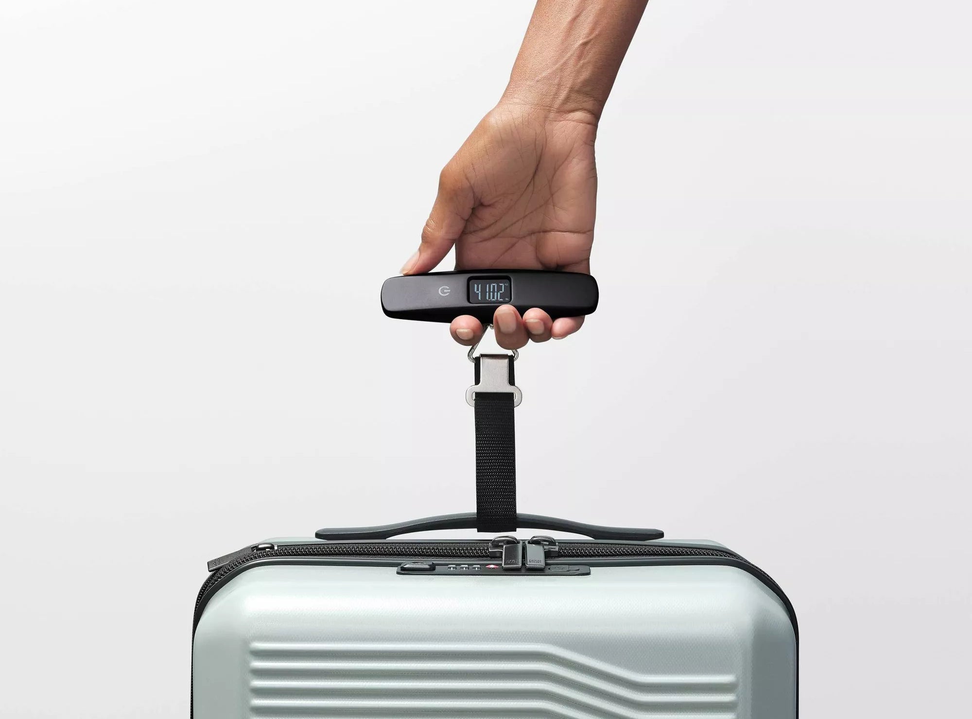 A hand holding the scale, which is attached to a piece of luggage