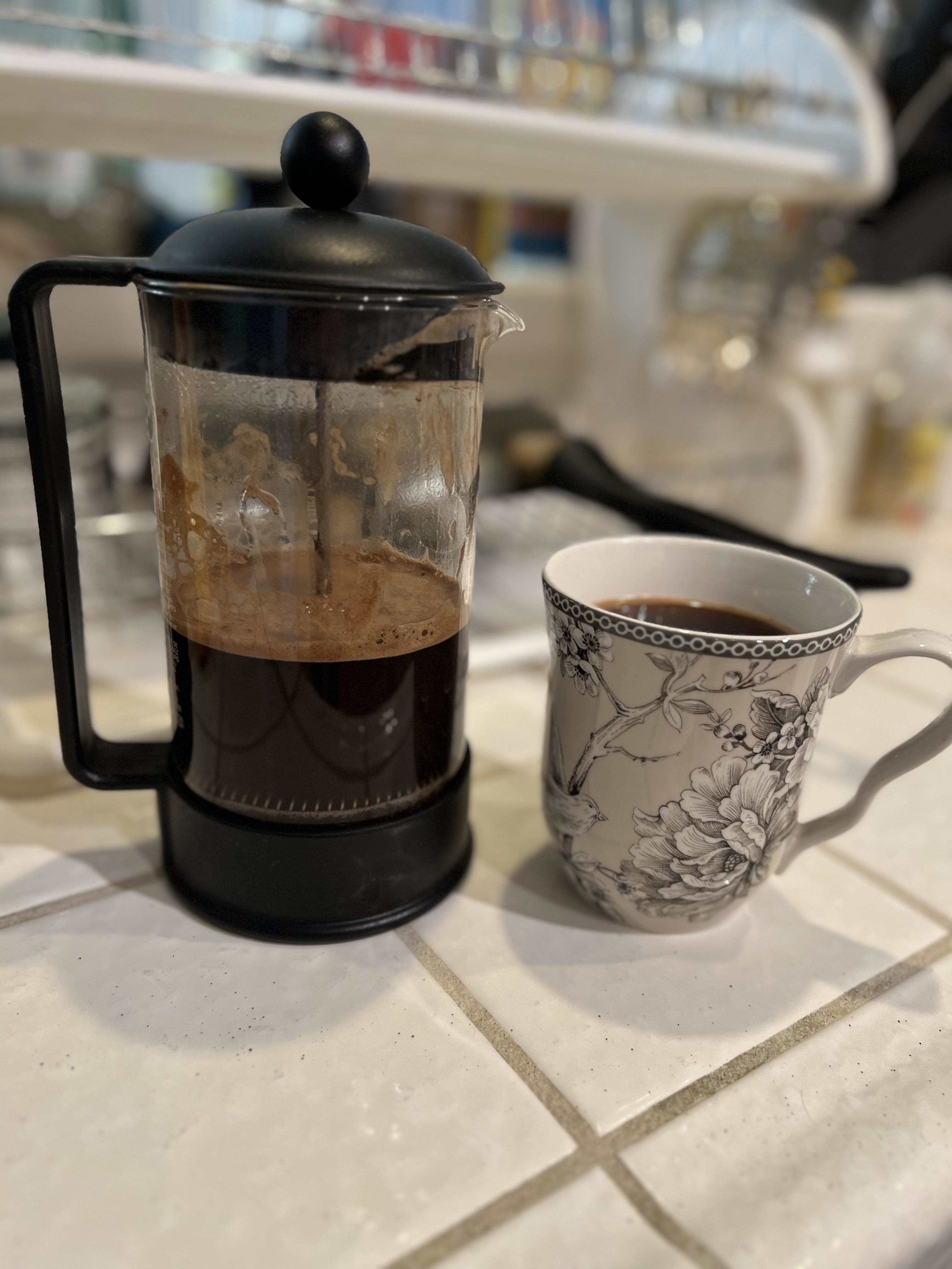 A French press with coffee next to a mug full of coffee