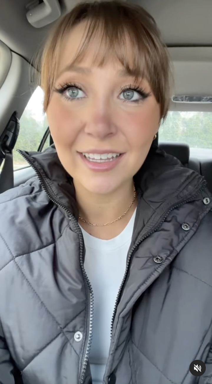 Devon in a car, wearing a zip-up jacket and a necklace