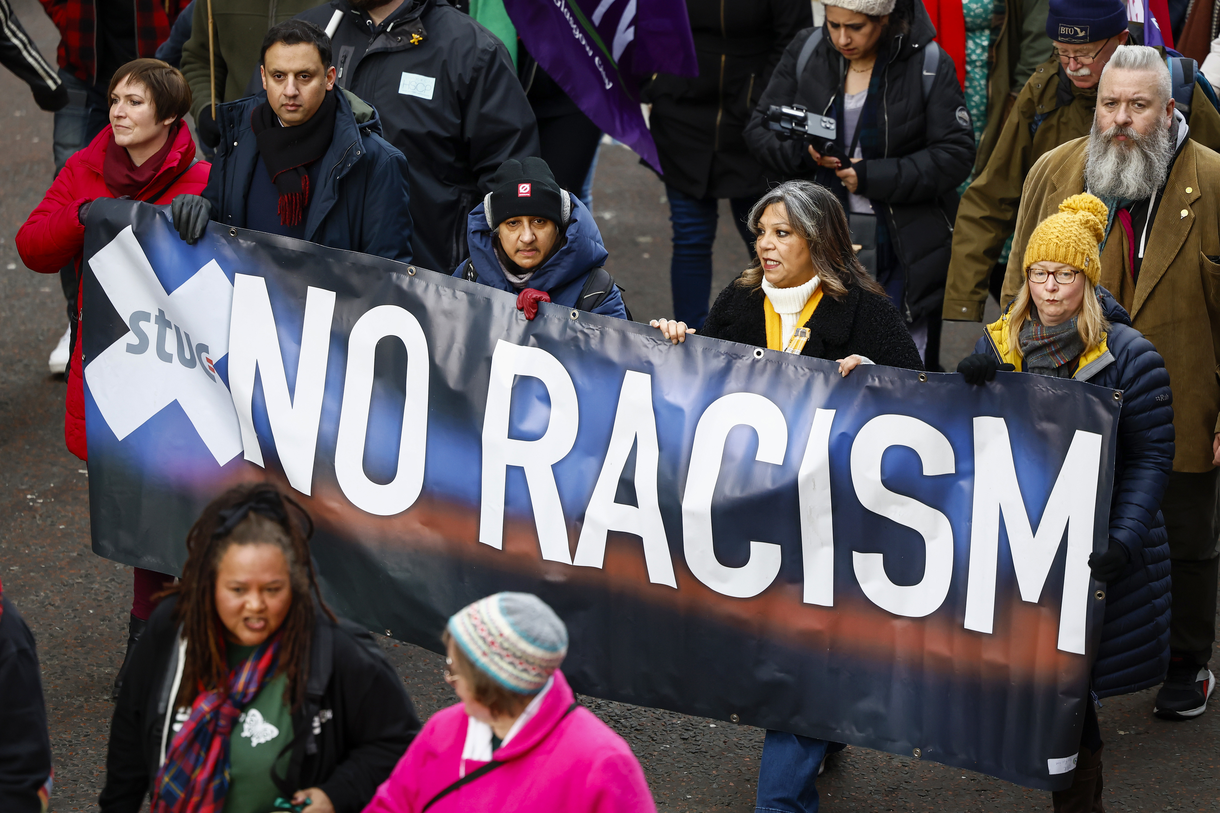 People hold up a &quot;No Racism&quot; banner at a rally